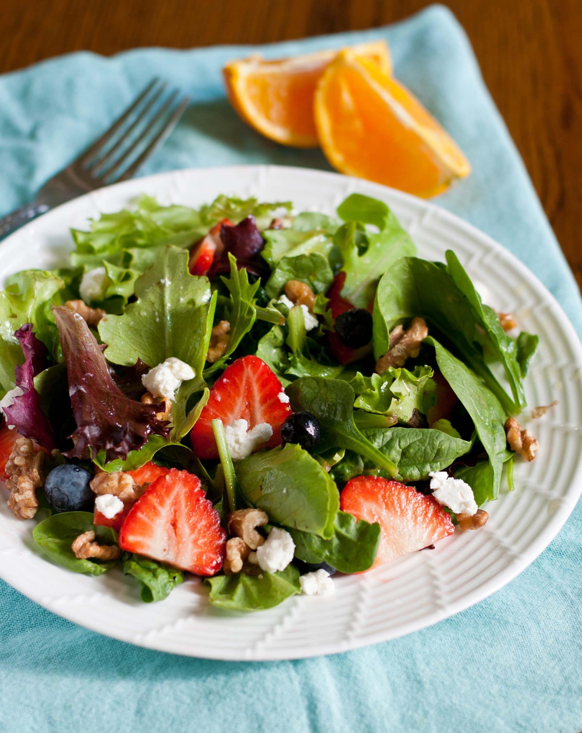 Goat cheese and walnut salad with mixed greens and berries on a white plate.