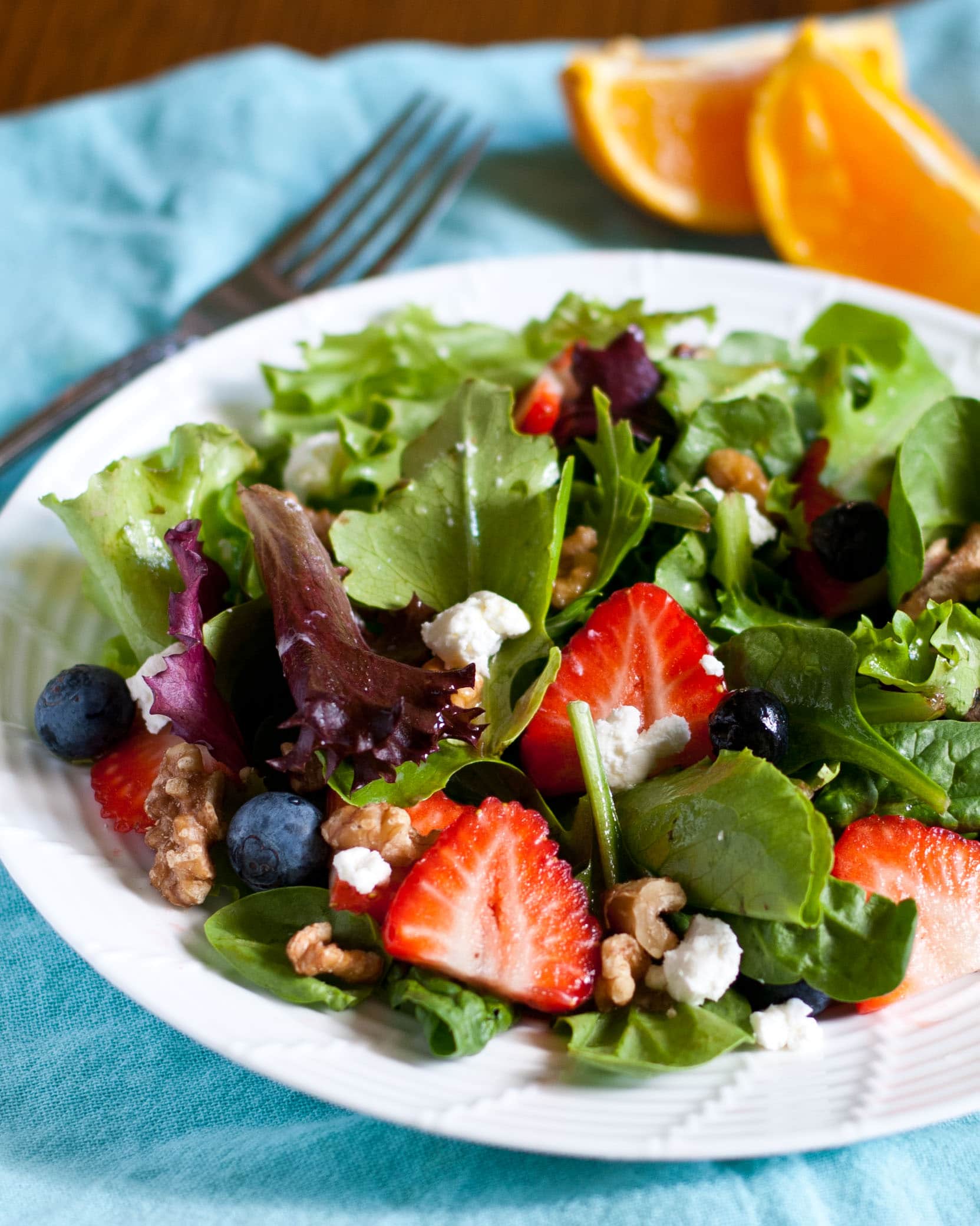 Salad with strawberries, blueberries, goat cheese, and walnuts on a white plate.