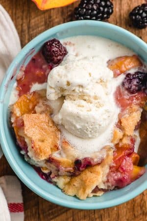 Scoop of blackberry peach cobbler in a blue bowl with a scoop of ice cream melting on top.
