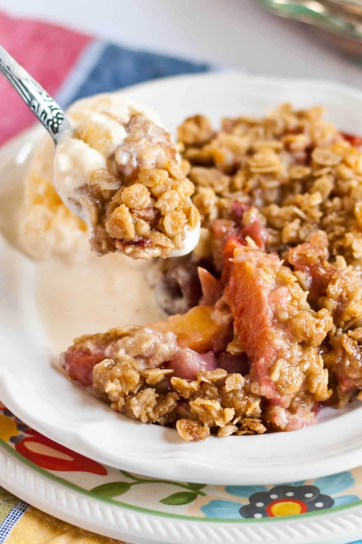 nectarine, strawberry, and cherry crisp being scooped with a spoon out of bowl.