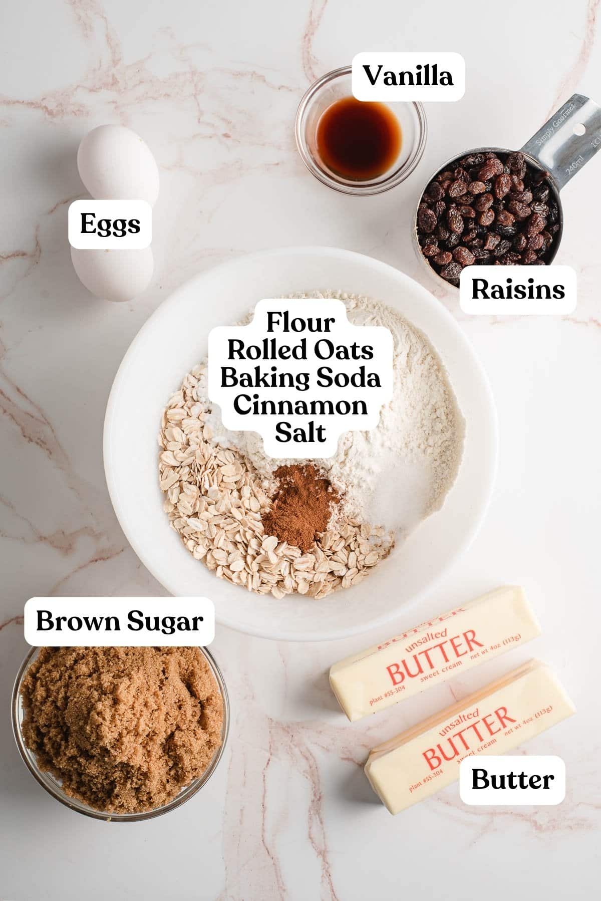 Bowl of flour, oats, cinnamon, baking soda, and salt, surrounded by bowls of raisins, eggs, vanilla, butter, brown sugar.