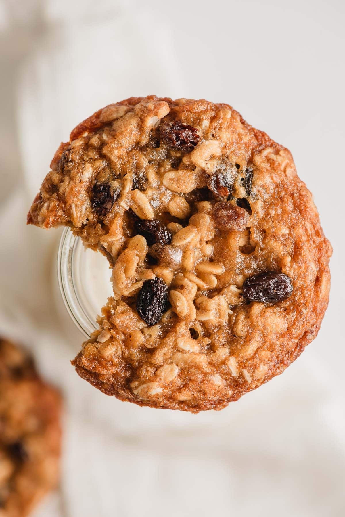 Old fashioned oatmeal raisin cookie balancing on a glass of milk, with a bite taken out of it.