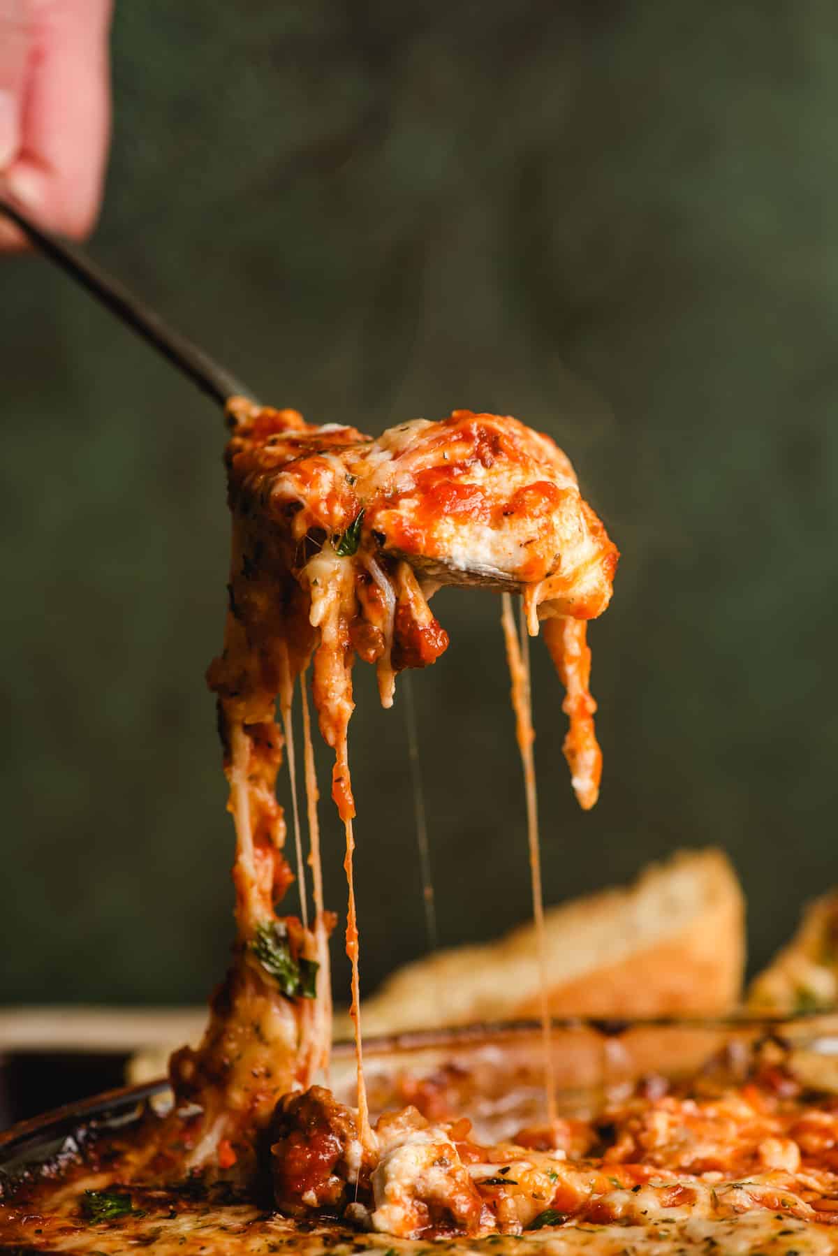 Spoon pulling a scoopful of lasagna dip from a dish, with strings of cheese trailing behind it.