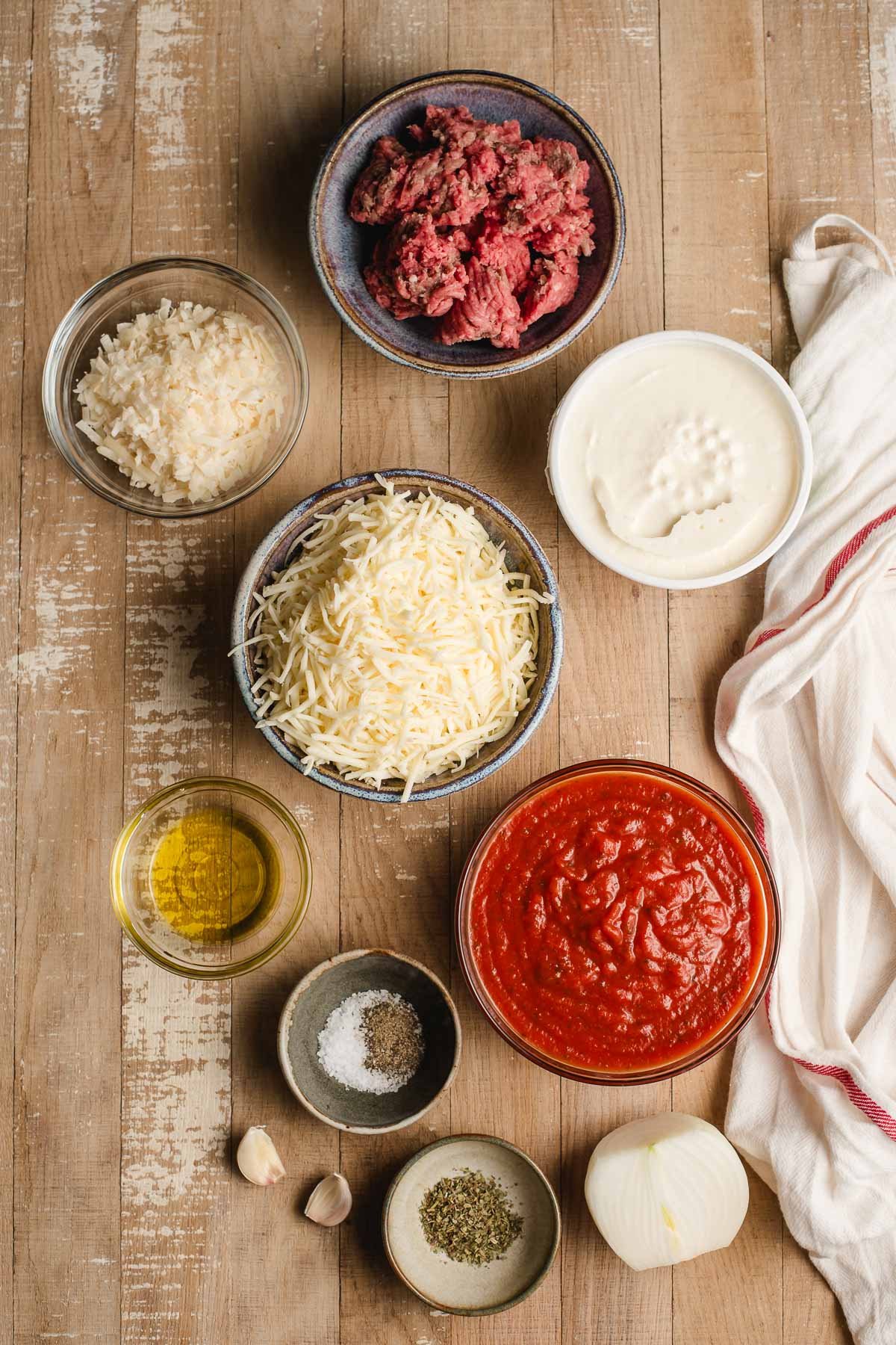 Ingredients for a lasagna dip in small bowls on a wood background.