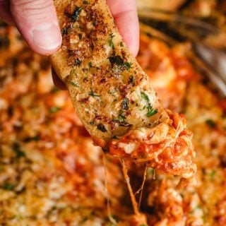 Garlic bread stick being dunked into a pan of lasagna dip.