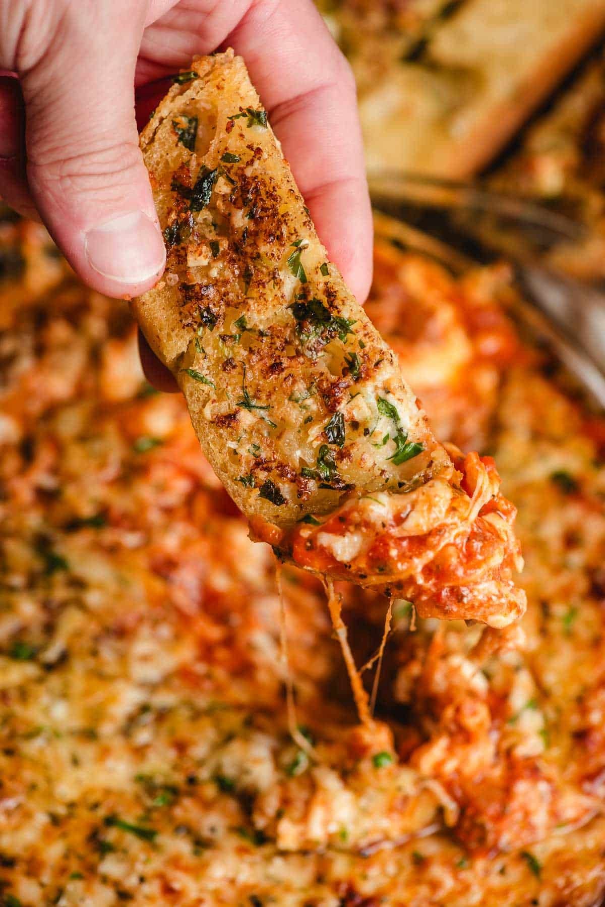 Garlic bread stick being dunked into a pan of lasagna dip.