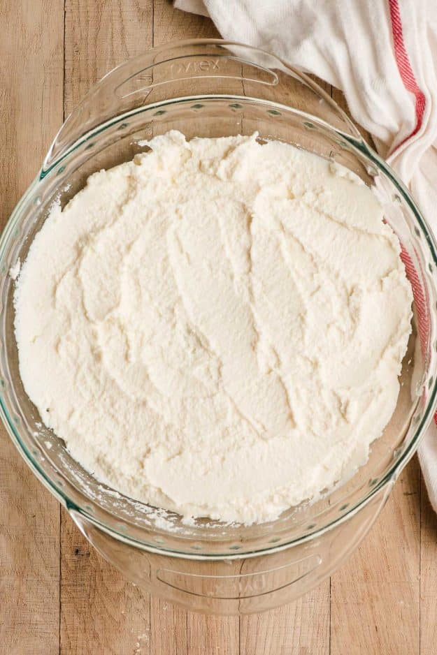 Ricotta cheese spread across the bottom of a pie dish.