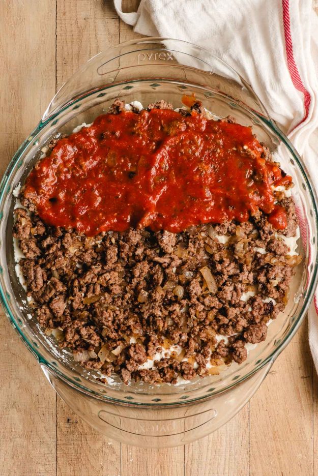 Sauteed ground beef and marinara sauce on top of ricotta cheese in a glass dish.