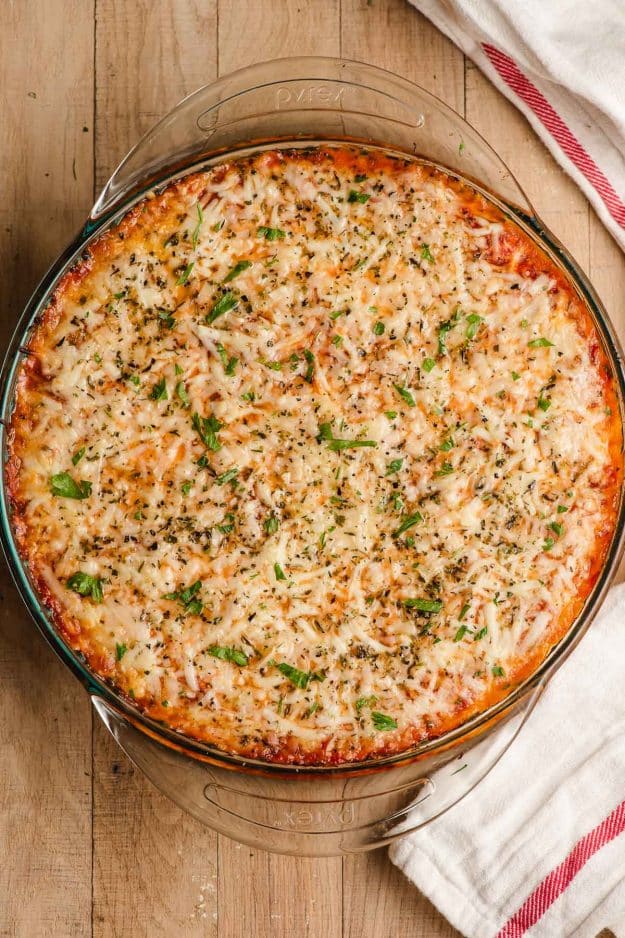 Baked lasagna dip in a round pie dish, sprinkled with basil.
