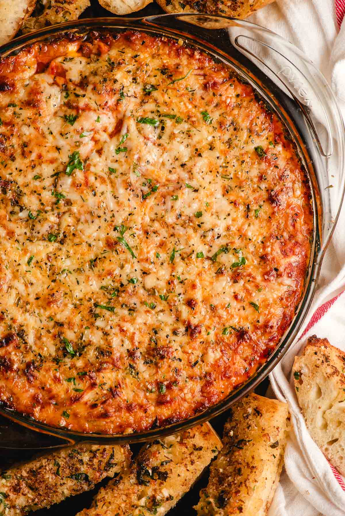 Hot baked lasagna dip in a glass pie dish with garlic bread dippers on the side.