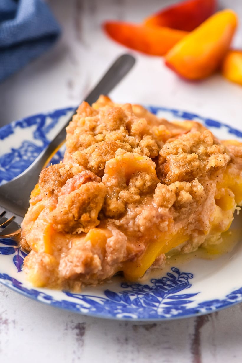 Slice of peach crumble pie on a white and blue plate