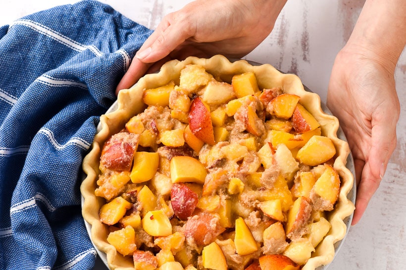 Hands holding an unbaked peach pie