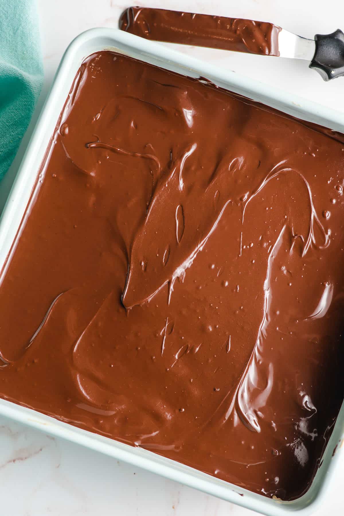 A layer of melted chocolate spread over a dessert in a square pan.