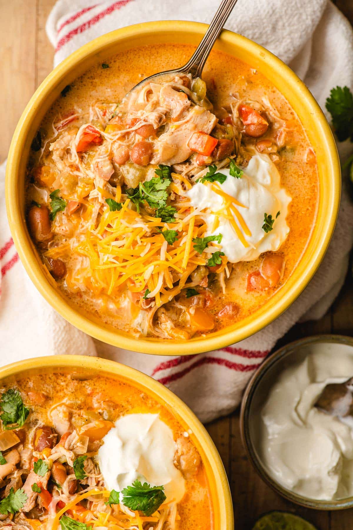 Crock pot white chicken chili in two yellow bowls, topped with sour cream and cheese.