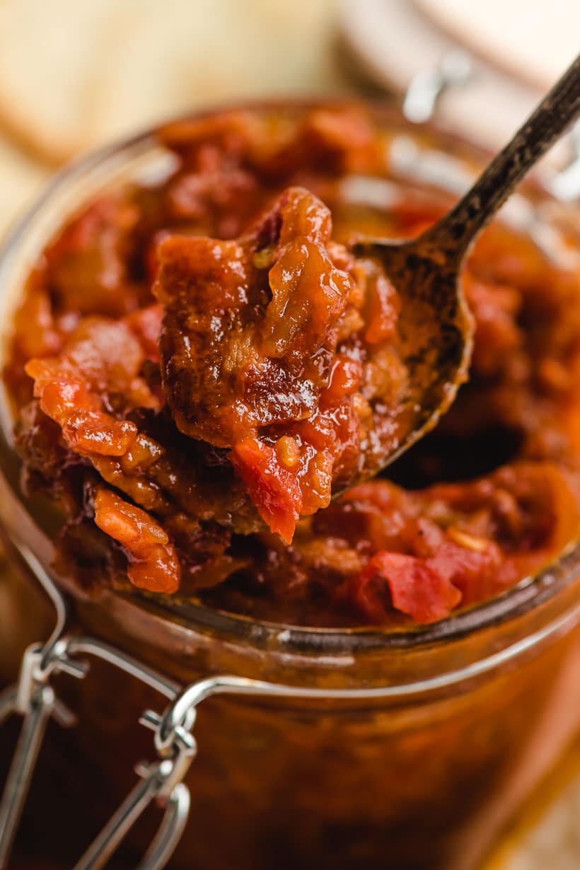 Jar of tomato bacon jam with a small spoon taking a scoop.