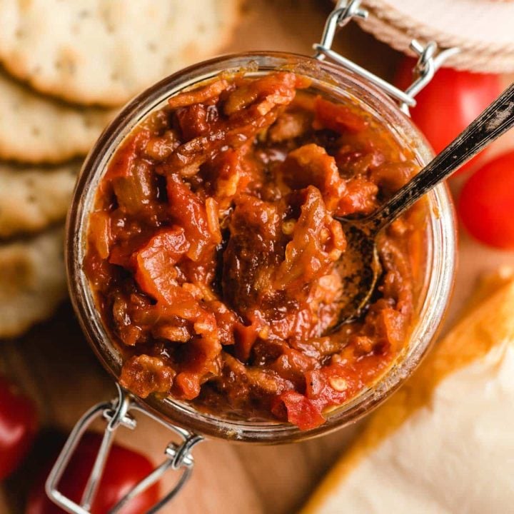 Up close image of a jar of tomato bacon jam with a small spoon in it.