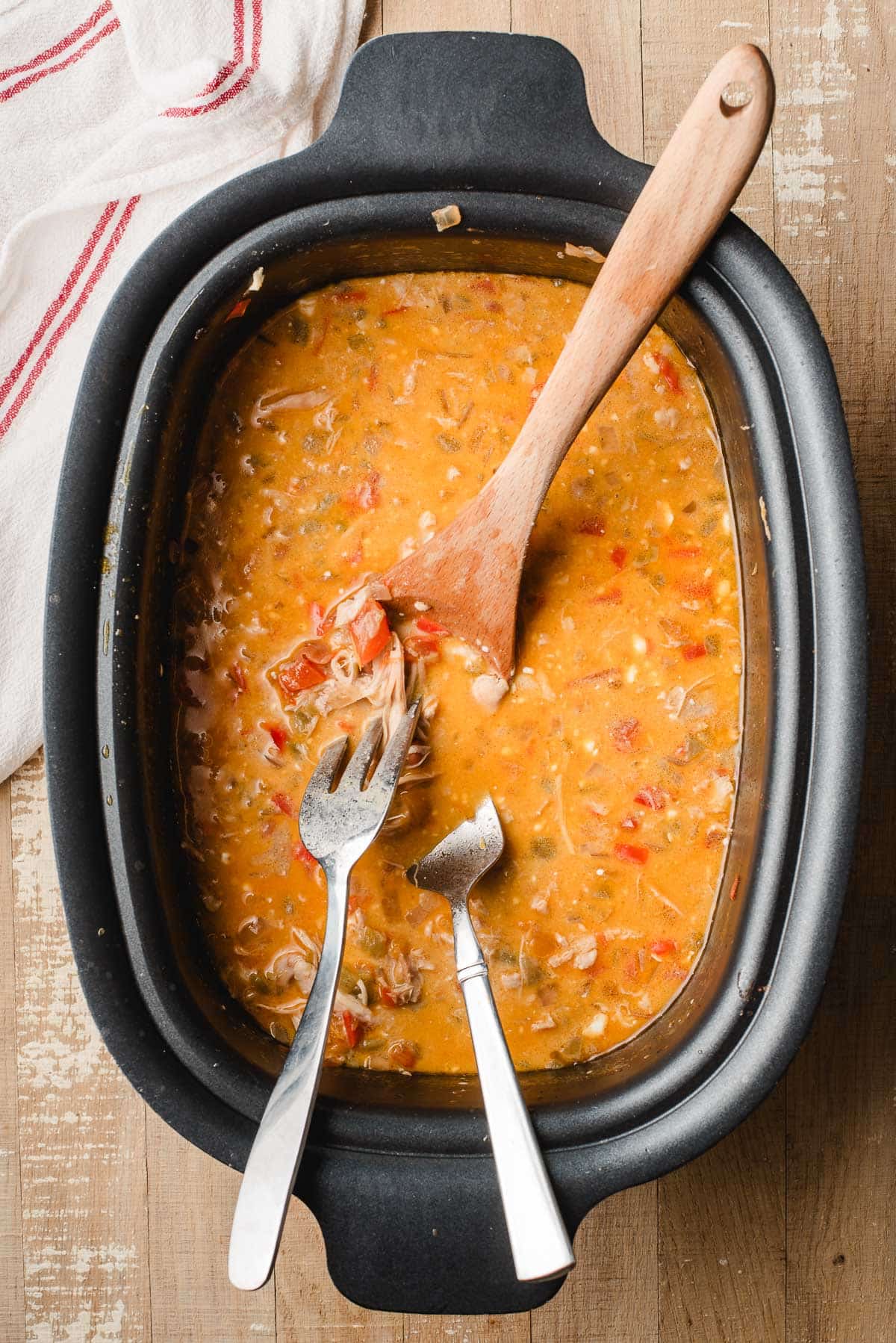Two forks shredding chicken in a crock pot with white chili.