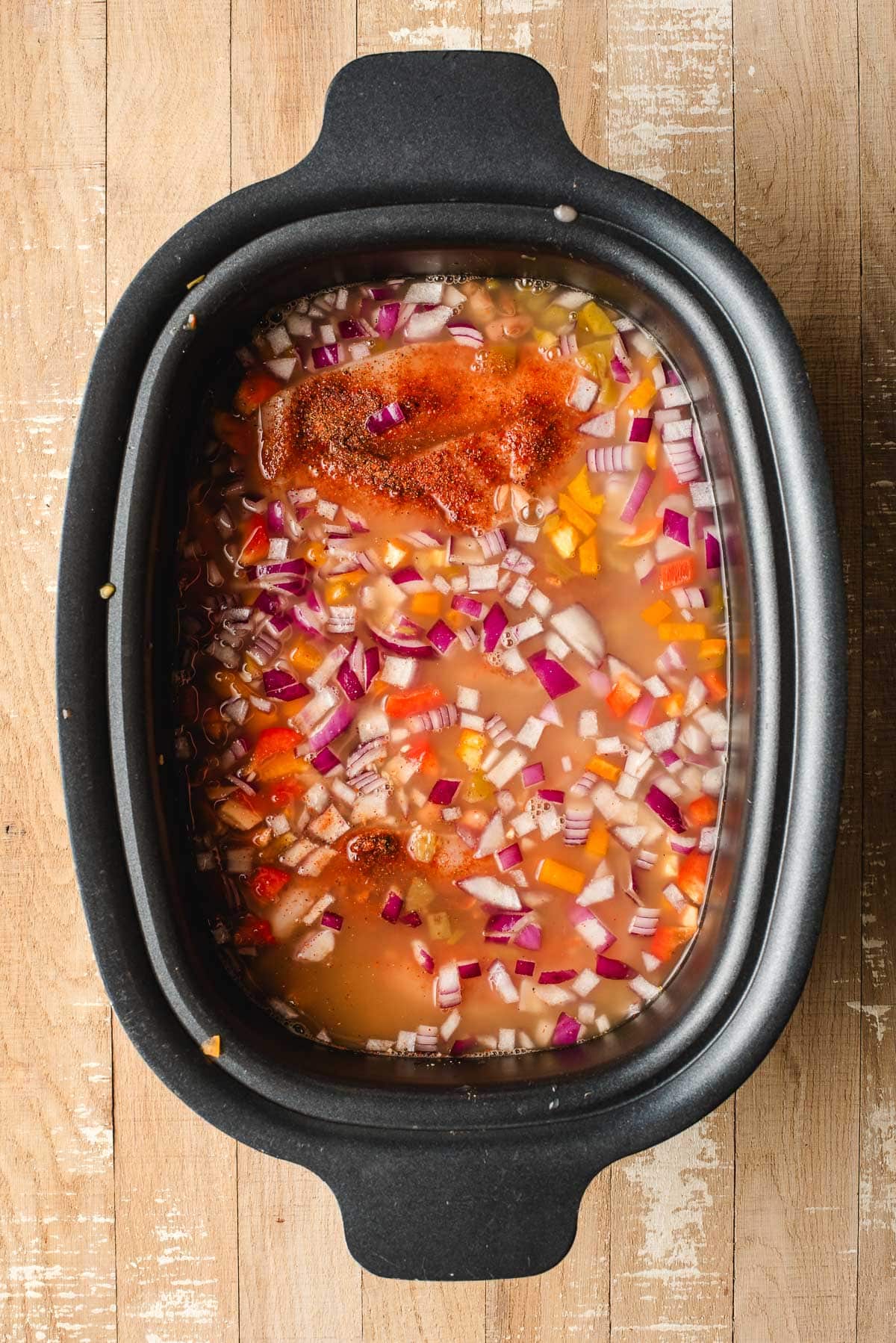 Bell peppers, onions, chicken, broth, beans, and seasonings in a crock pot.
