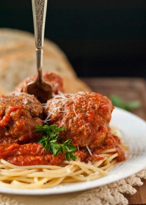 Three large Italian meatballs in homemade tomato sauce on top of spaghetti noodles.