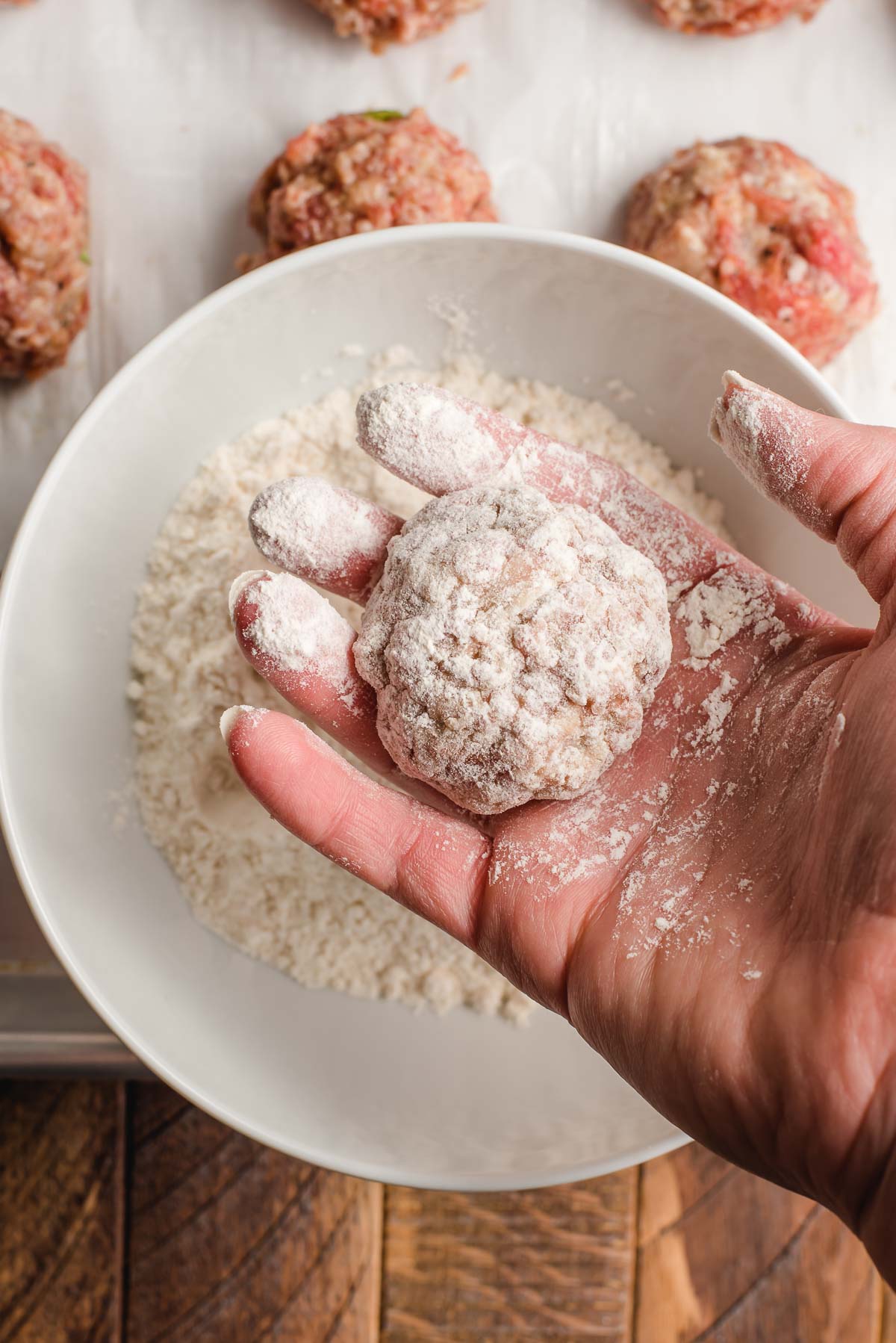 Hand holding a meatball dredged in flour before frying.