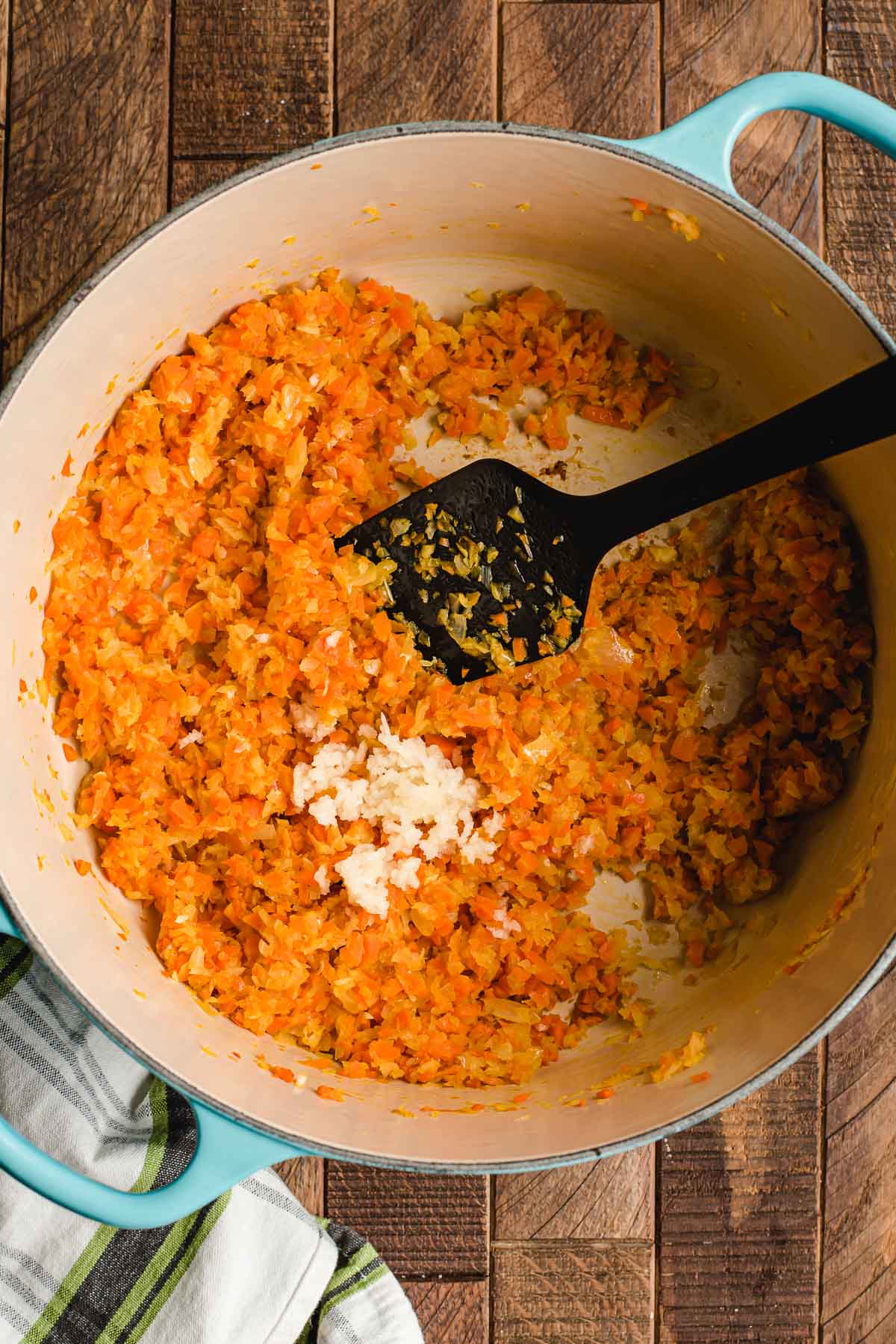 Fresh minced garlic shown on top of sauteed carrots and onions in a skillet.