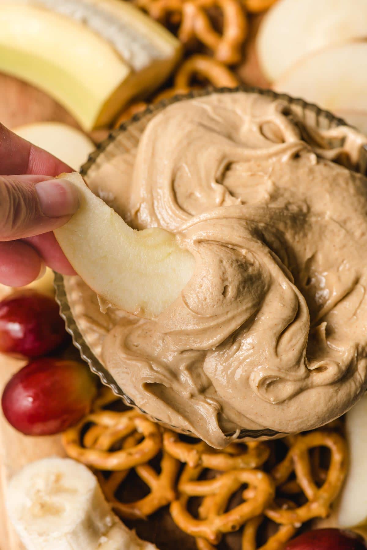 Hand dipping a slice of apple into a bowl of Amish peanut butter spread.
