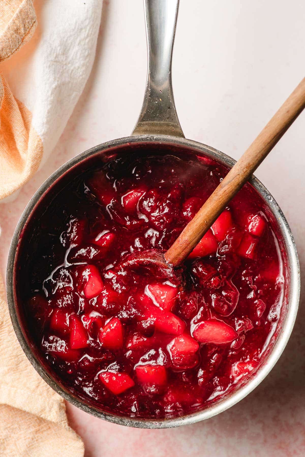 Cranberry pear sauce stirred with a wooden spoon in a saucepan.