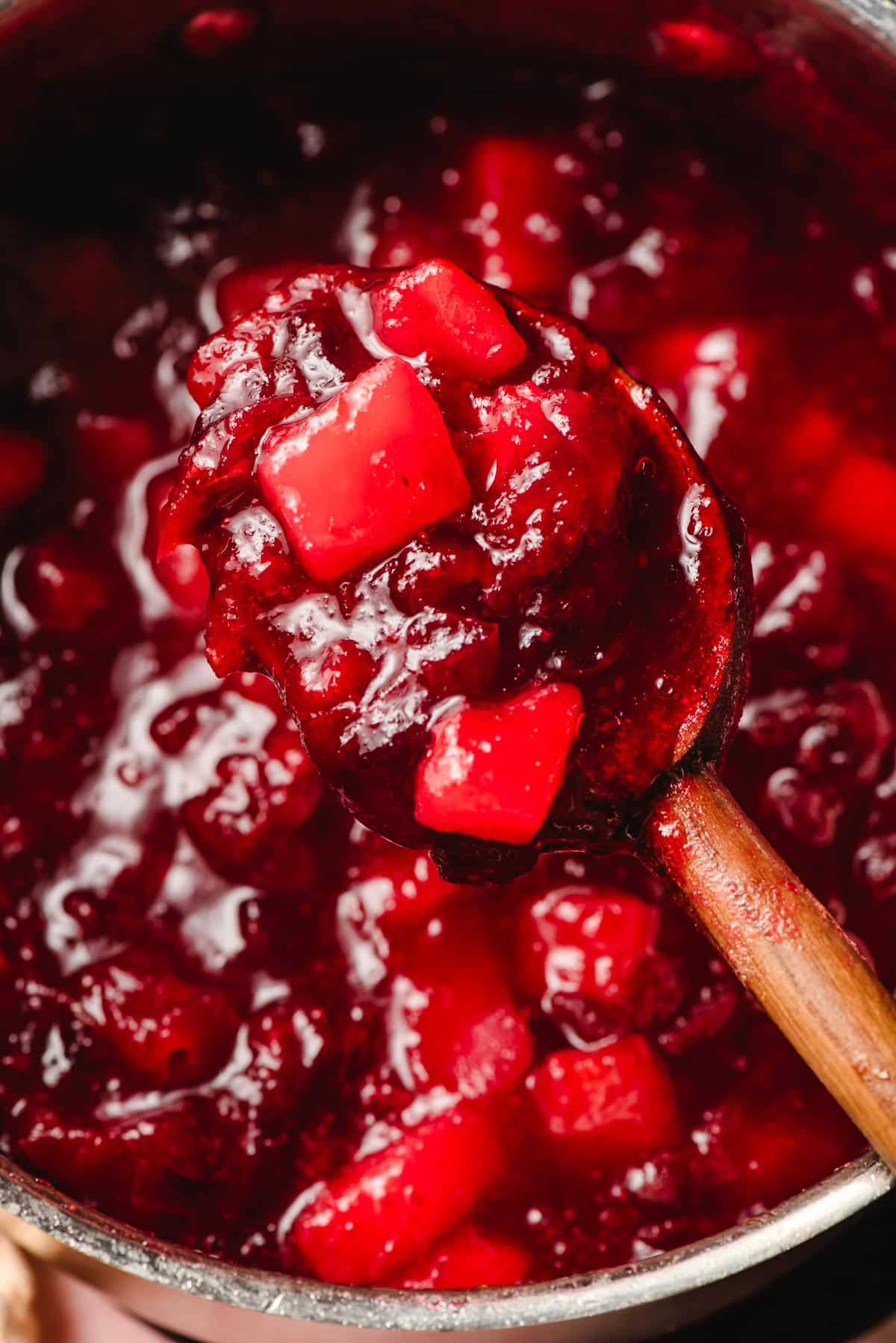 Wooden spoon scooping up homemade cranberry pear sauce from a saucepan.
