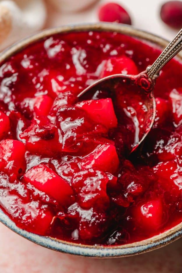 Spoon scooping up homemade cranberry pear sauce out of a glazed bowl.