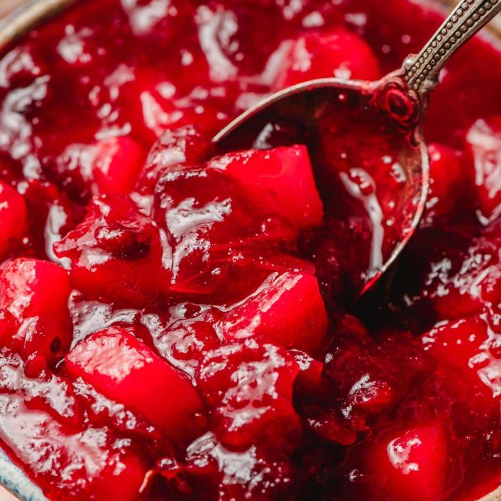 Spoon scooping up homemade cranberry pear sauce out of a glazed bowl.