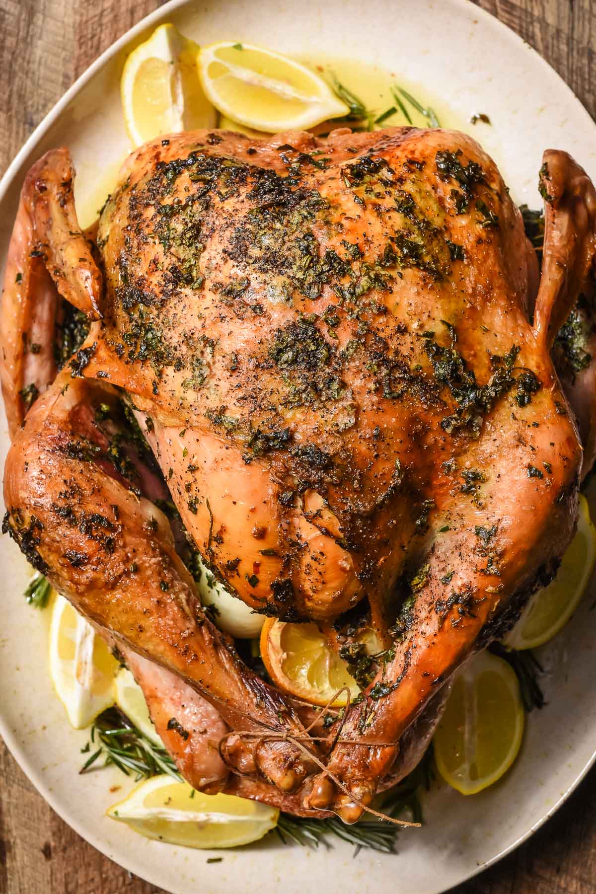 Garlic and herb roasted turkey on a large platter surrounded by sliced lemons and herbs.