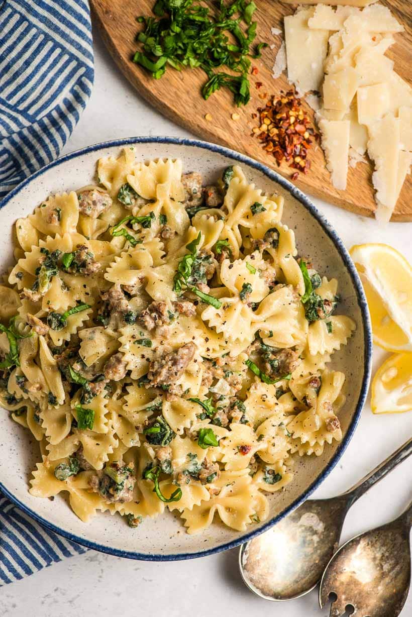 sausage pasta with kale in a white bowl with Parmesan cheese