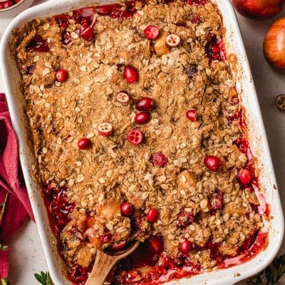Apple cranberry crisp in a baking dish with a wooden spoon.