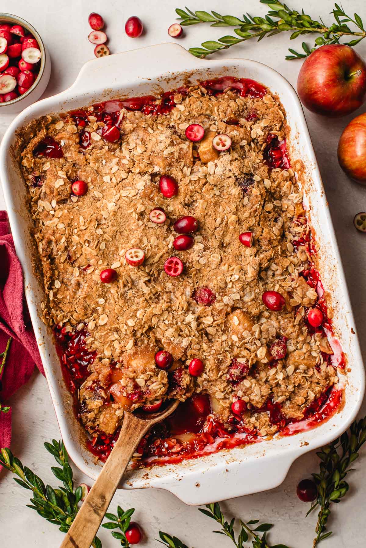 Apple cranberry crisp in a baking dish with a wooden spoon.