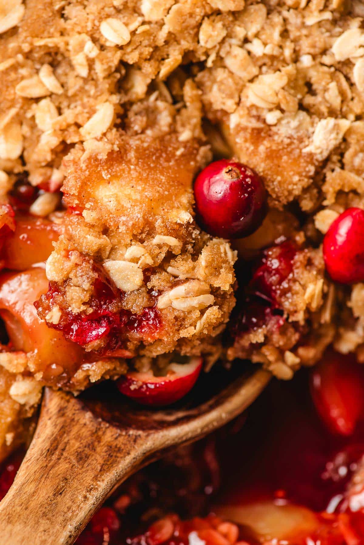 Wooden spoon scooping up apple cranberry crisp.