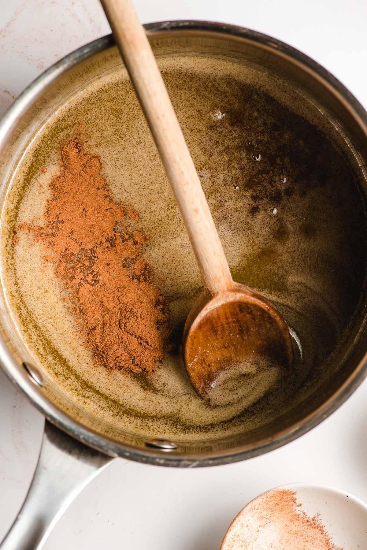 Cinnamon added to a sauce pot with caramel sauce.