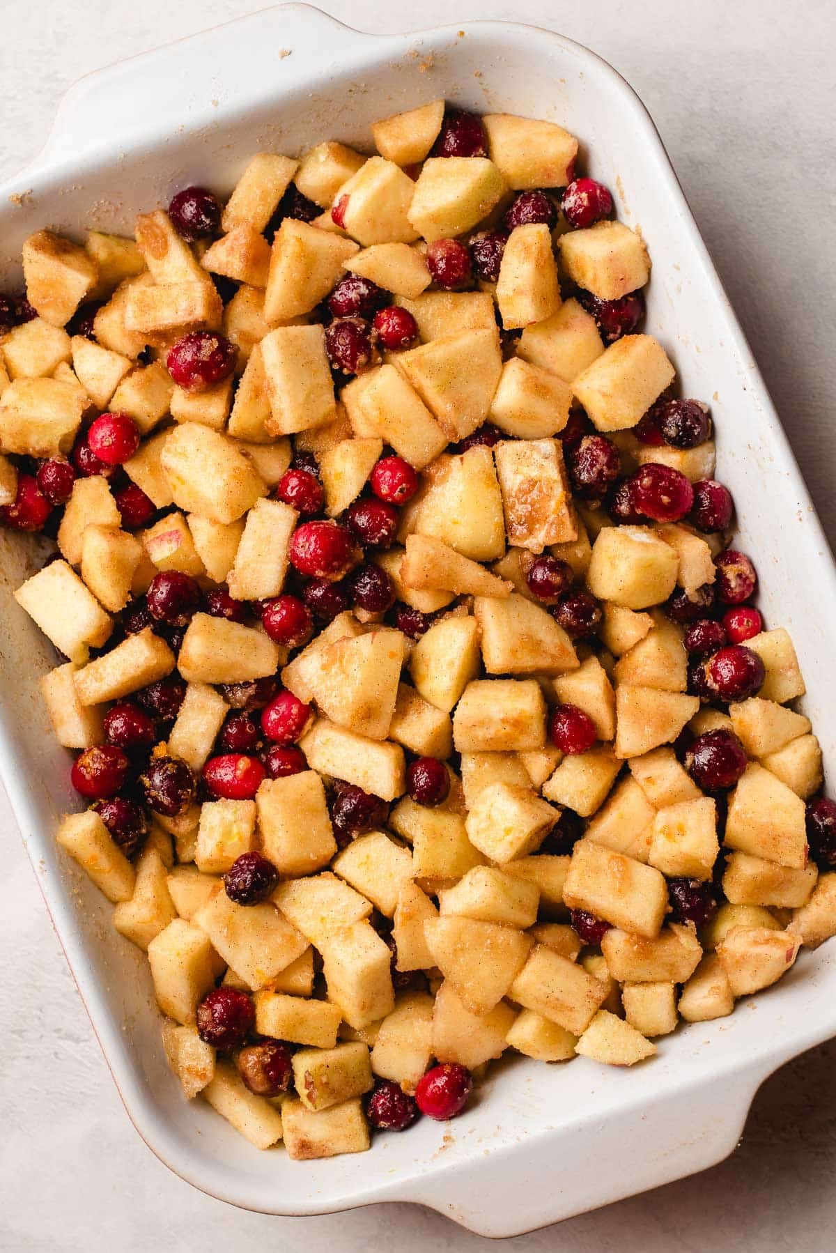 Apples and cranberries tossed with flour and spices in a baking dish.