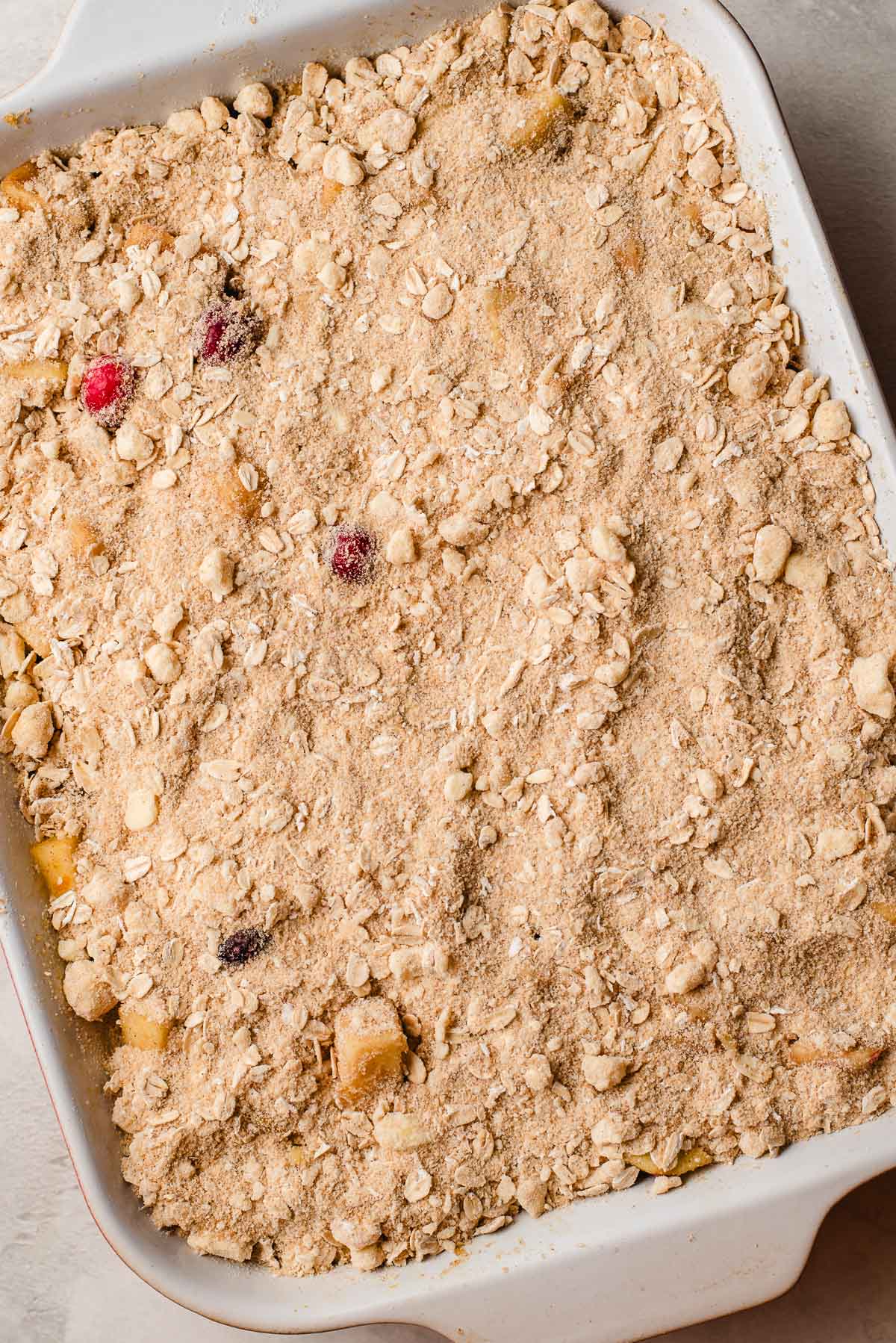 Buttery crumble on top of a cranberry apple filling in a baking pan.