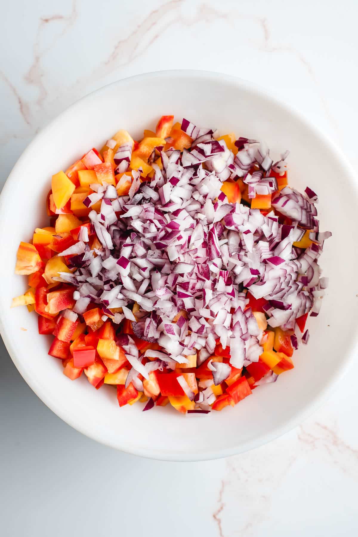 White bowl filled with black beans, kidney beans, cannelini beans, bell pepper, red onion, and cilantro.