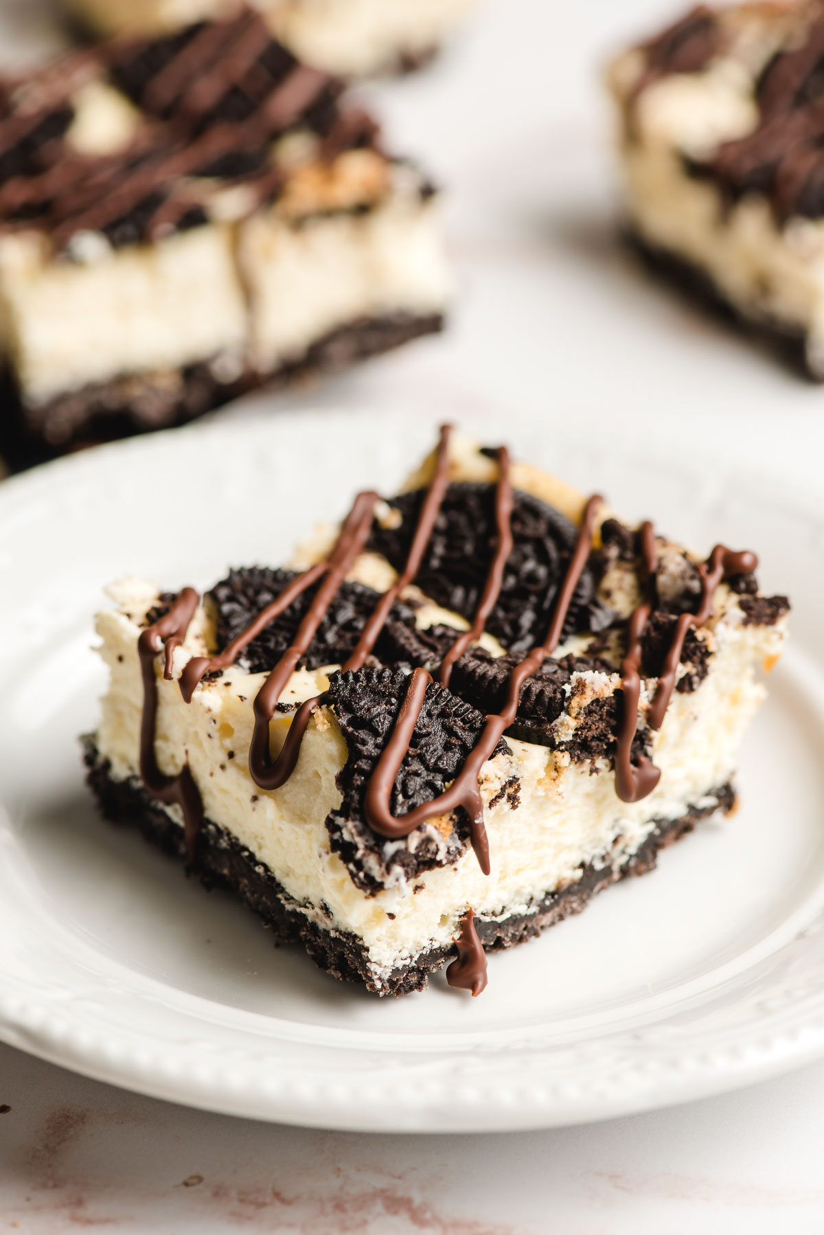 Oreo Cheesecake Bar topped with whole oreos and a drizzle of chocolate on a white plate.