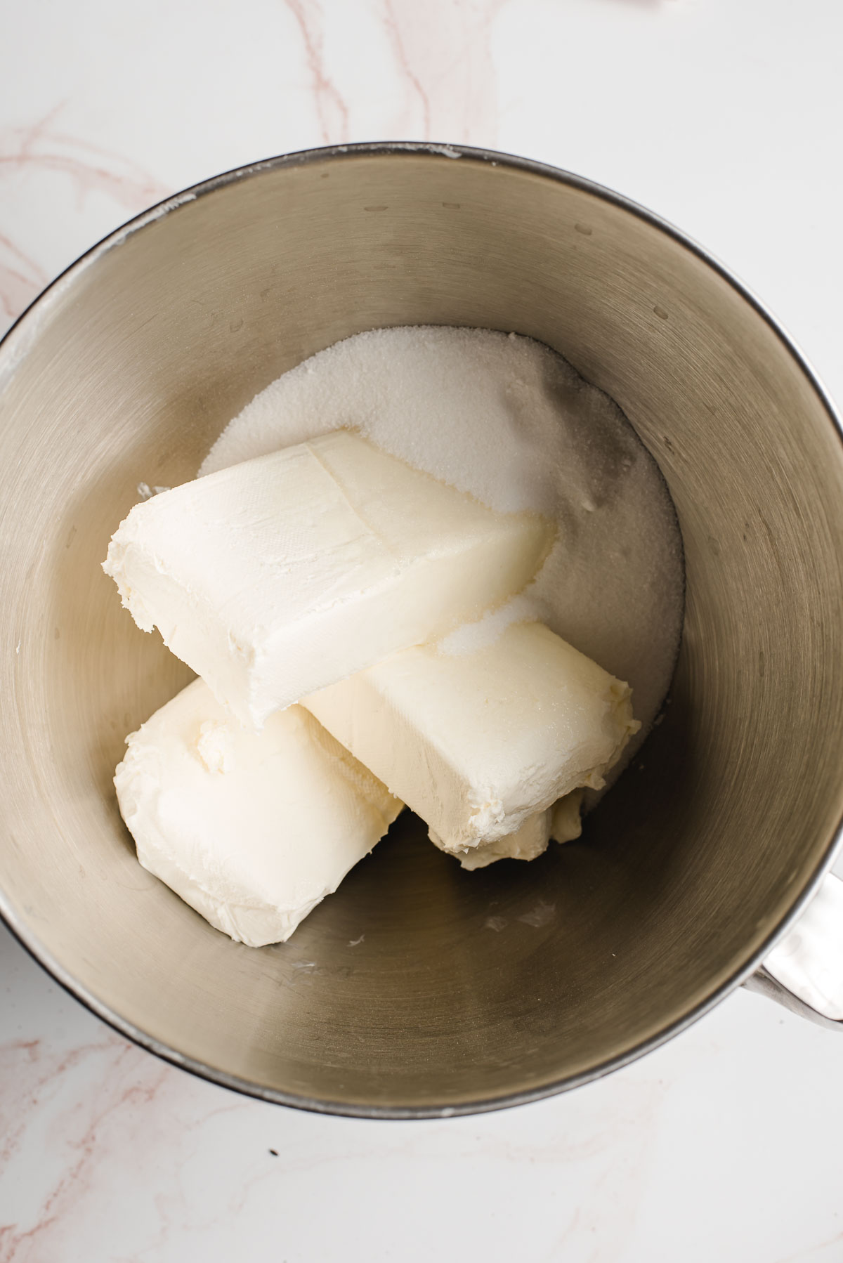 Blocks of cream cheese and sugar in the bowl of an electric mixer.
