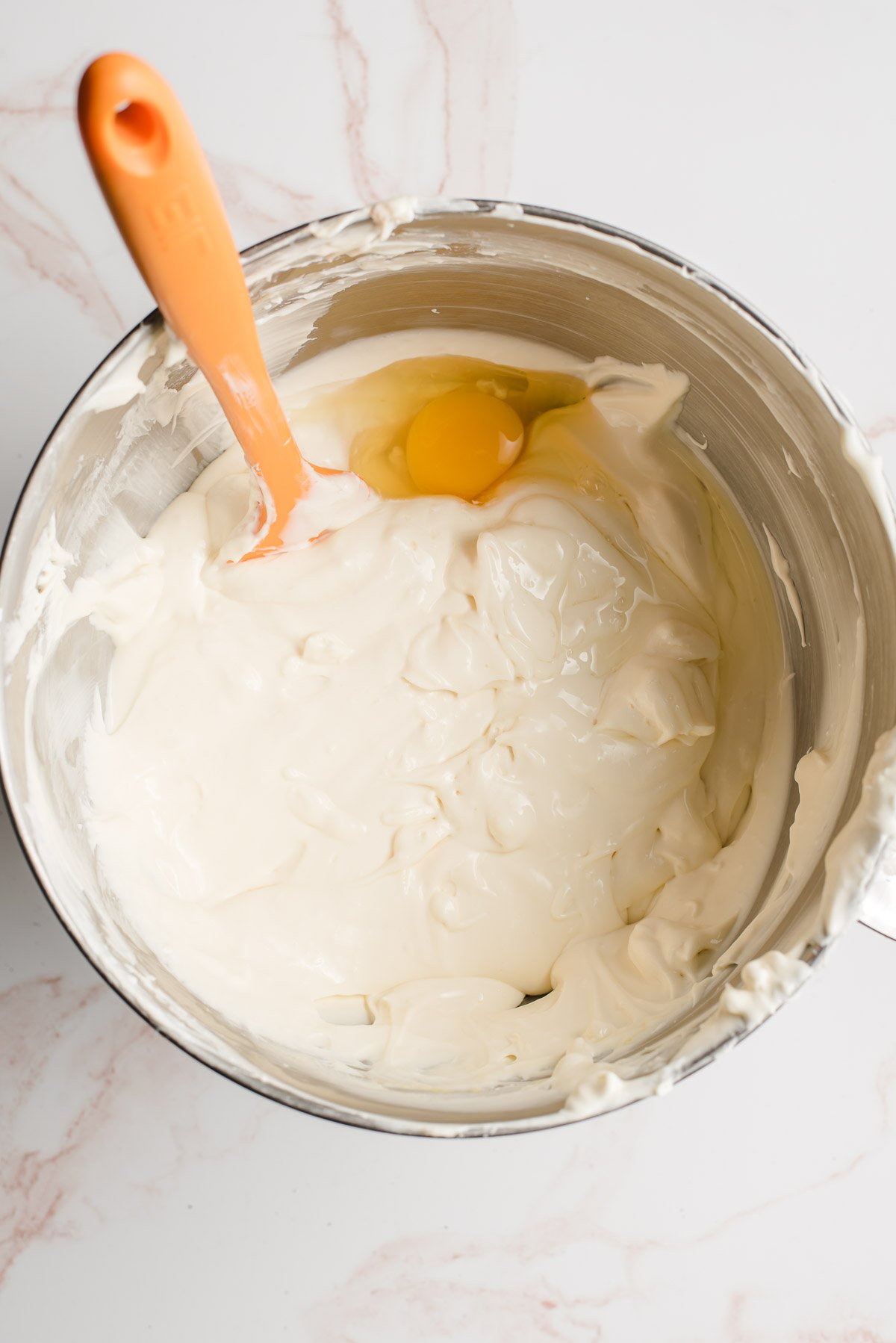 Electric mixer bowl with cream cheese, sugar, and egg.