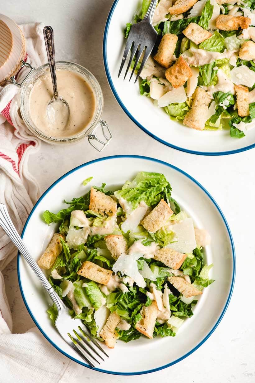 Two Caesar salads in white bowls with blue rims.