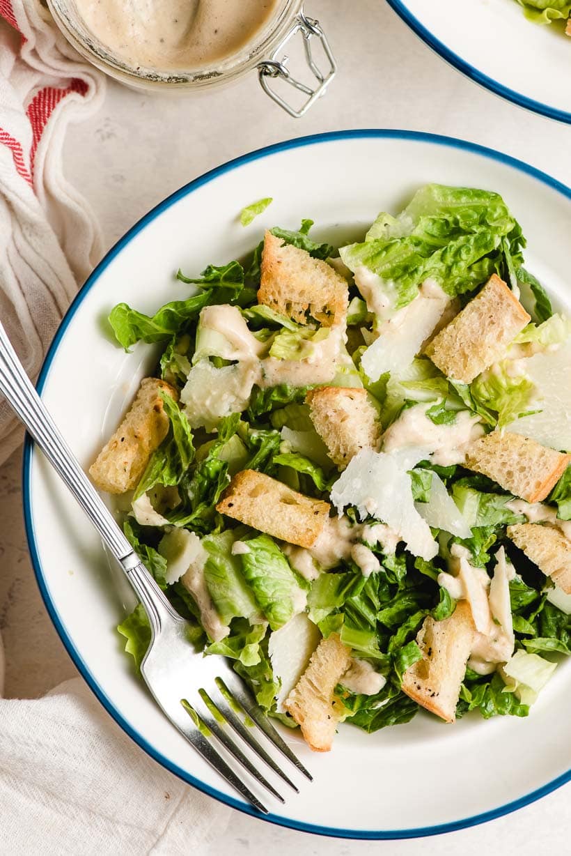 A blue rimmed white bowl holding a Caesar salad with croutons and shaved Parmesan.