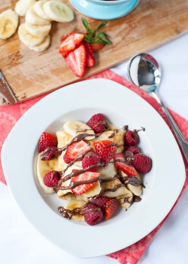 White plate with Ice Cream Crepes topped with strawberries and nutella.