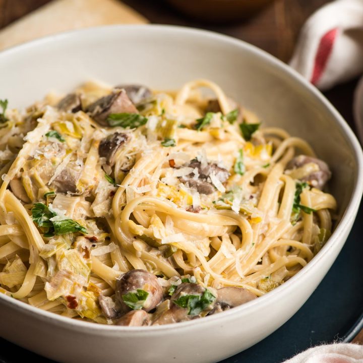 White bowl filled with linguine, mushrooms, and leeks in a creamy sauce.