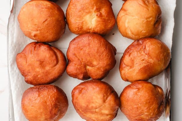 Fried paczkis lined up on a baking sheet.