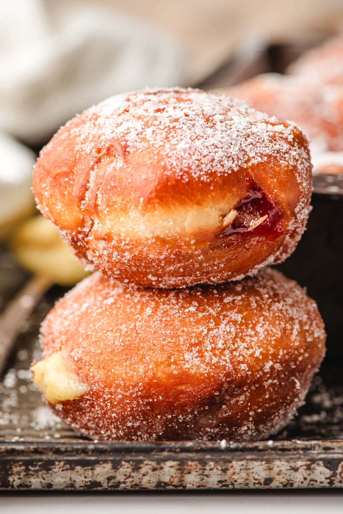 Stack of custard and strawberry paczki on a metal baking sheet.