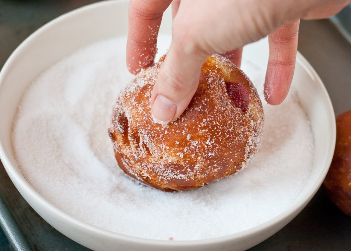 Paczki being dipped into granulated sugar.
