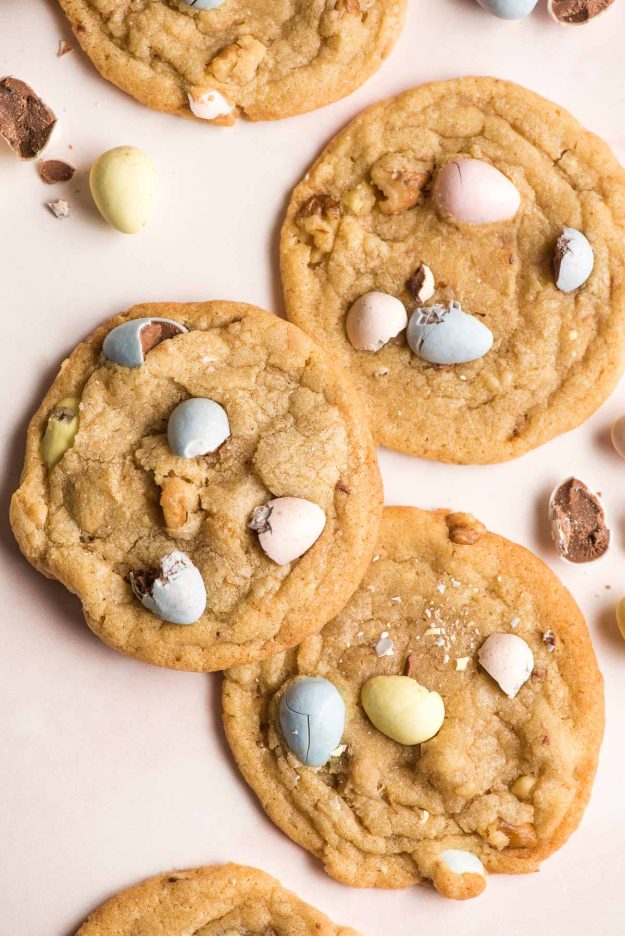 Mini egg cookies with broken pieces of cadbury mini eggs shown around them.
